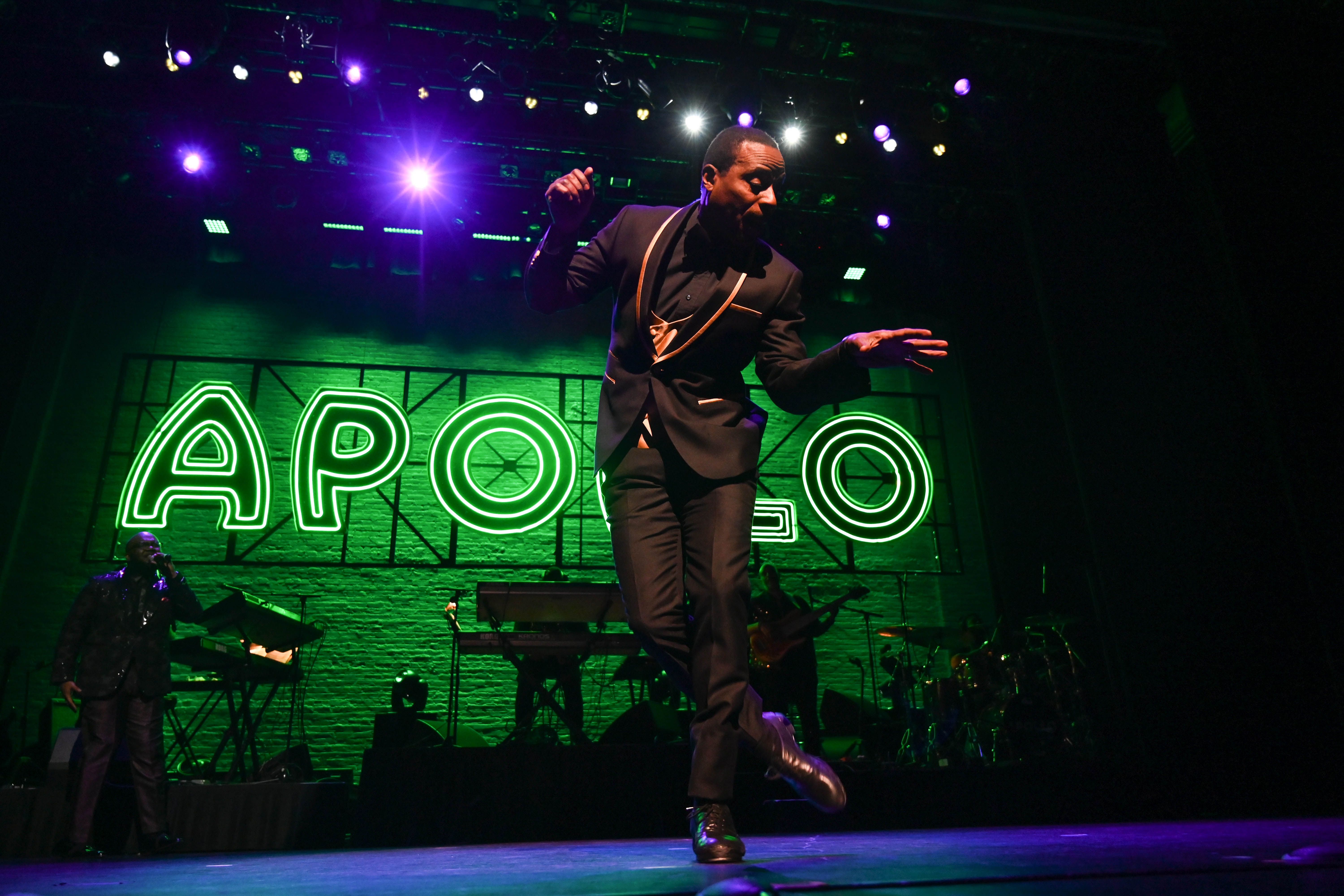 Image of Apollo Amateur Night Executioner, C.P. Lacey, wearing a black suit dancing on stage in front of a green neon sign reading the word Apollo.